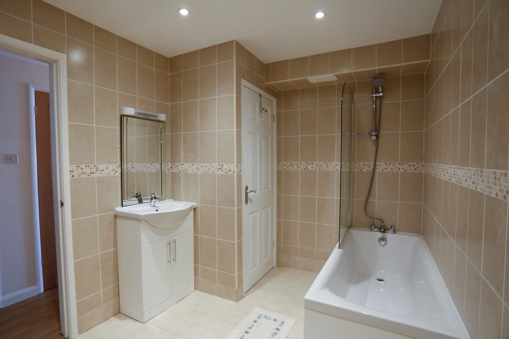 Bathroom with bath, shower and shower screen. Wash basin with mirror above.